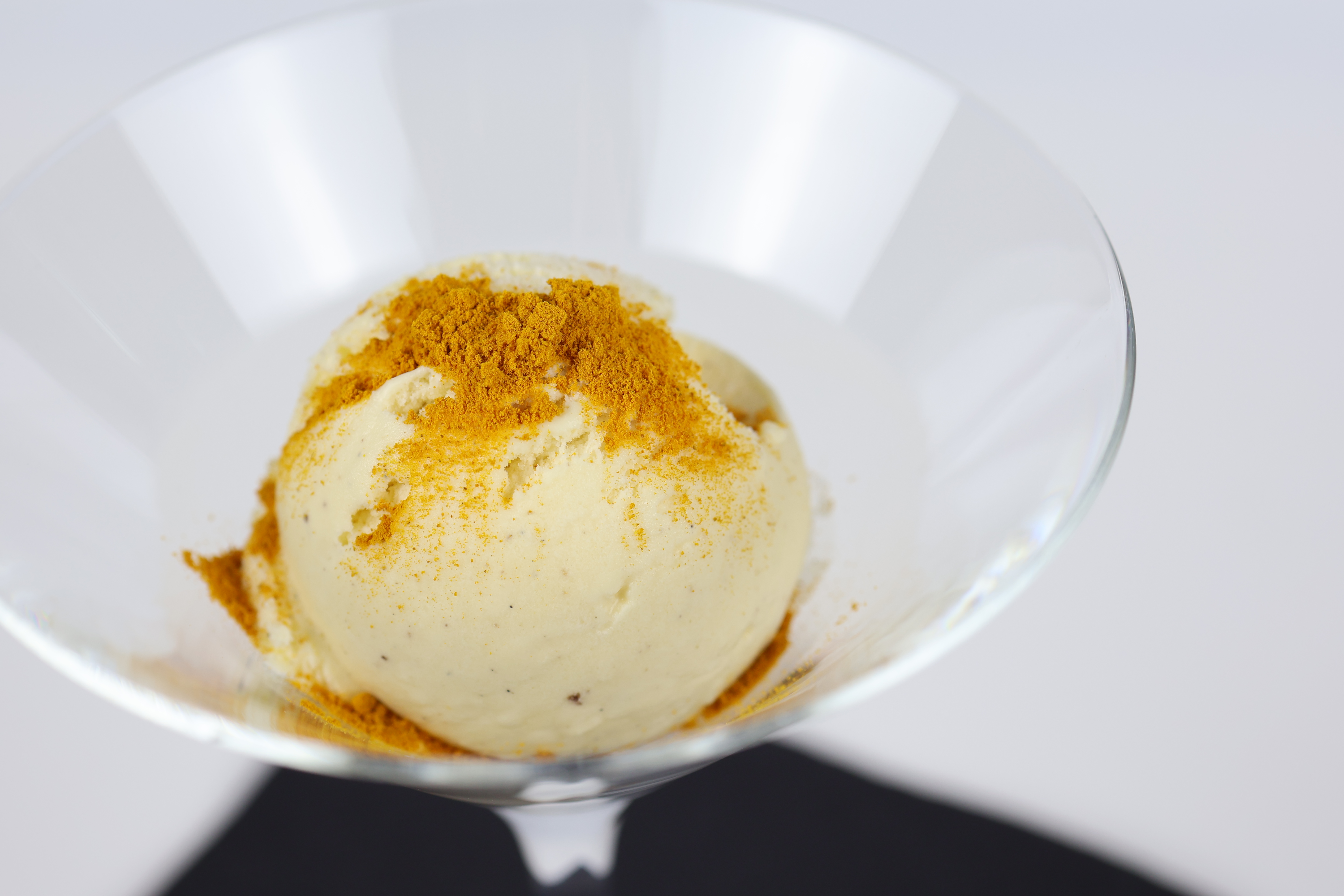 Kugel Vanilleeis in einem Glas mit einer Prise gelbem Gewürzpulver bestreut