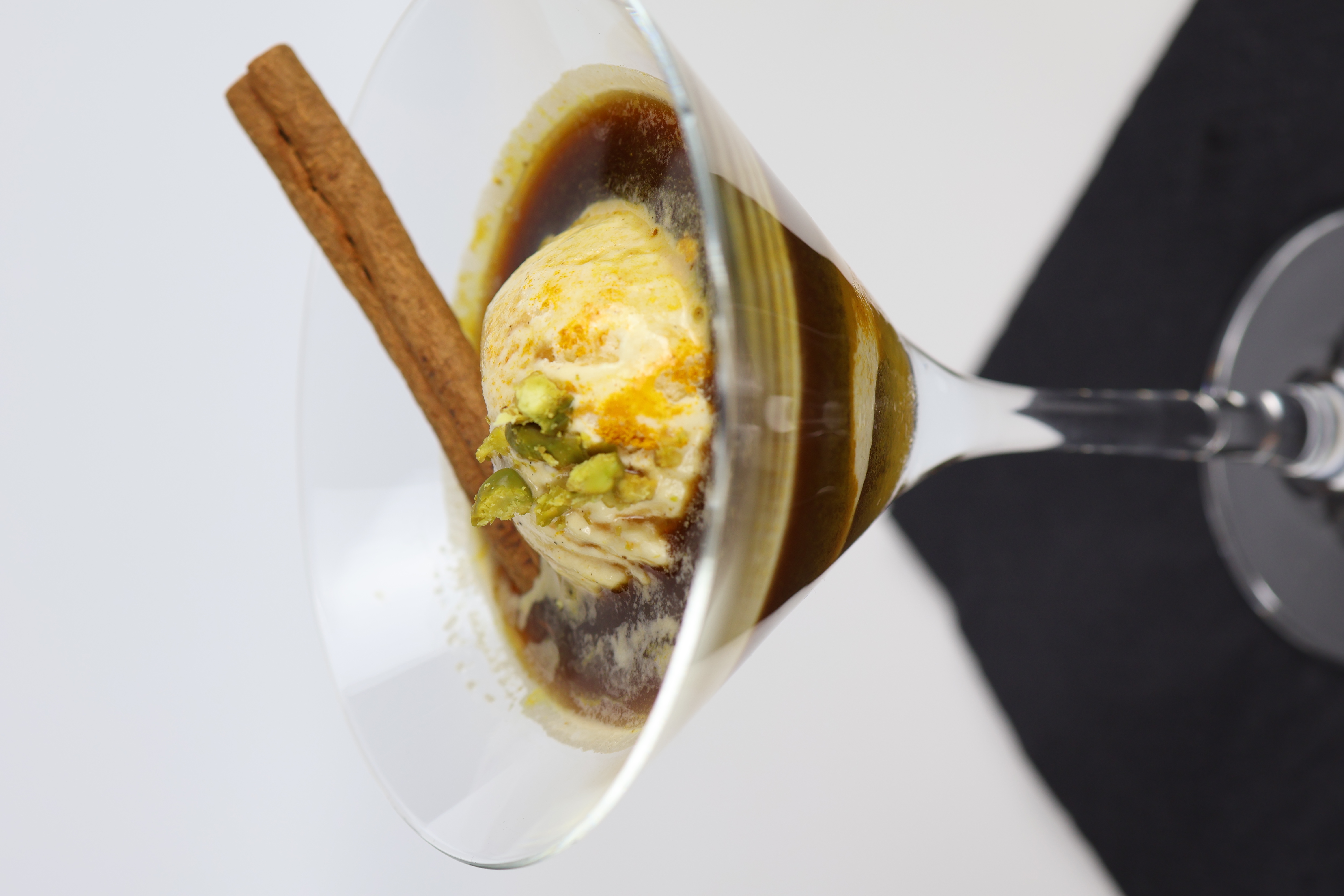 Cocktailglas mit dunklem Getränk, einer Kugel Vanilleeis, Pistazienstückchen und einer Zimtstange
