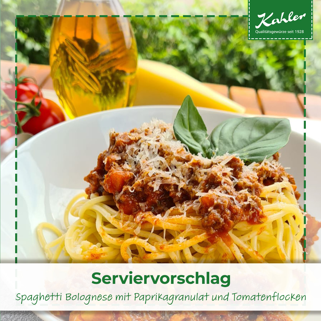 Spaghetti Bolognese mit Paprikagranulat und Tomatenflocken auf weißem Teller garniert mit Basilikumblatt und im Hintergrund Ölflasche und Tomaten, oben ein Kahler Logo