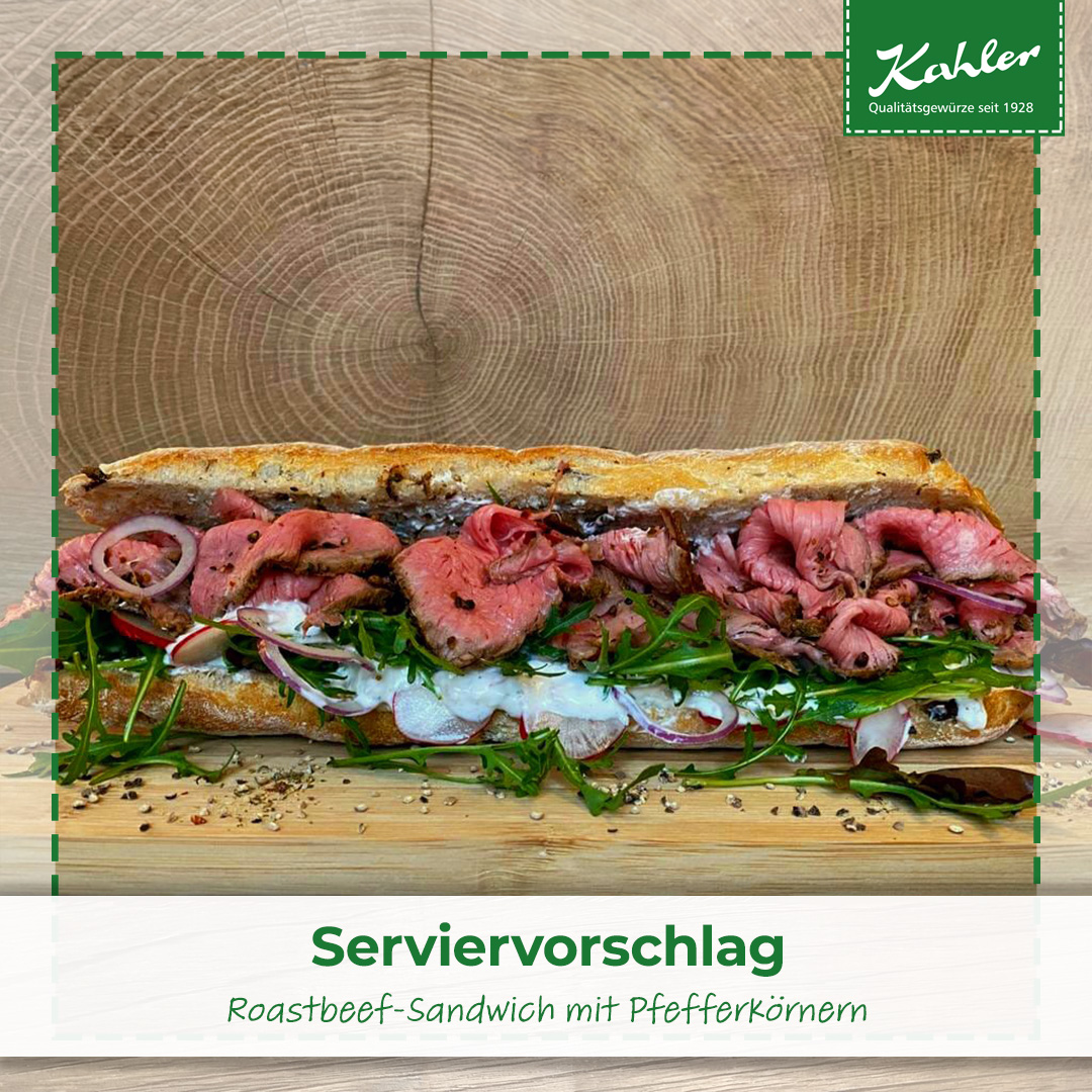 Roastbeef-Sandwich mit Rucola, Zwiebeln und Pfefferkörnern auf Holzbrett vor Baumstammquerschnitt und Kahler Logo