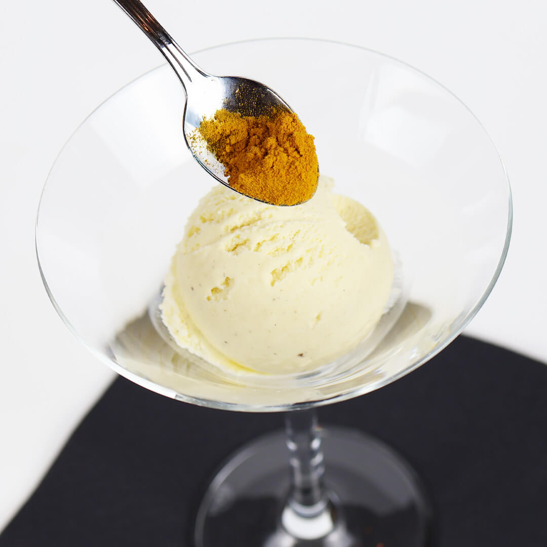 Eiskugel in einem Cocktailglas mit einem Löffel, der Kurkumapulver darüber hält