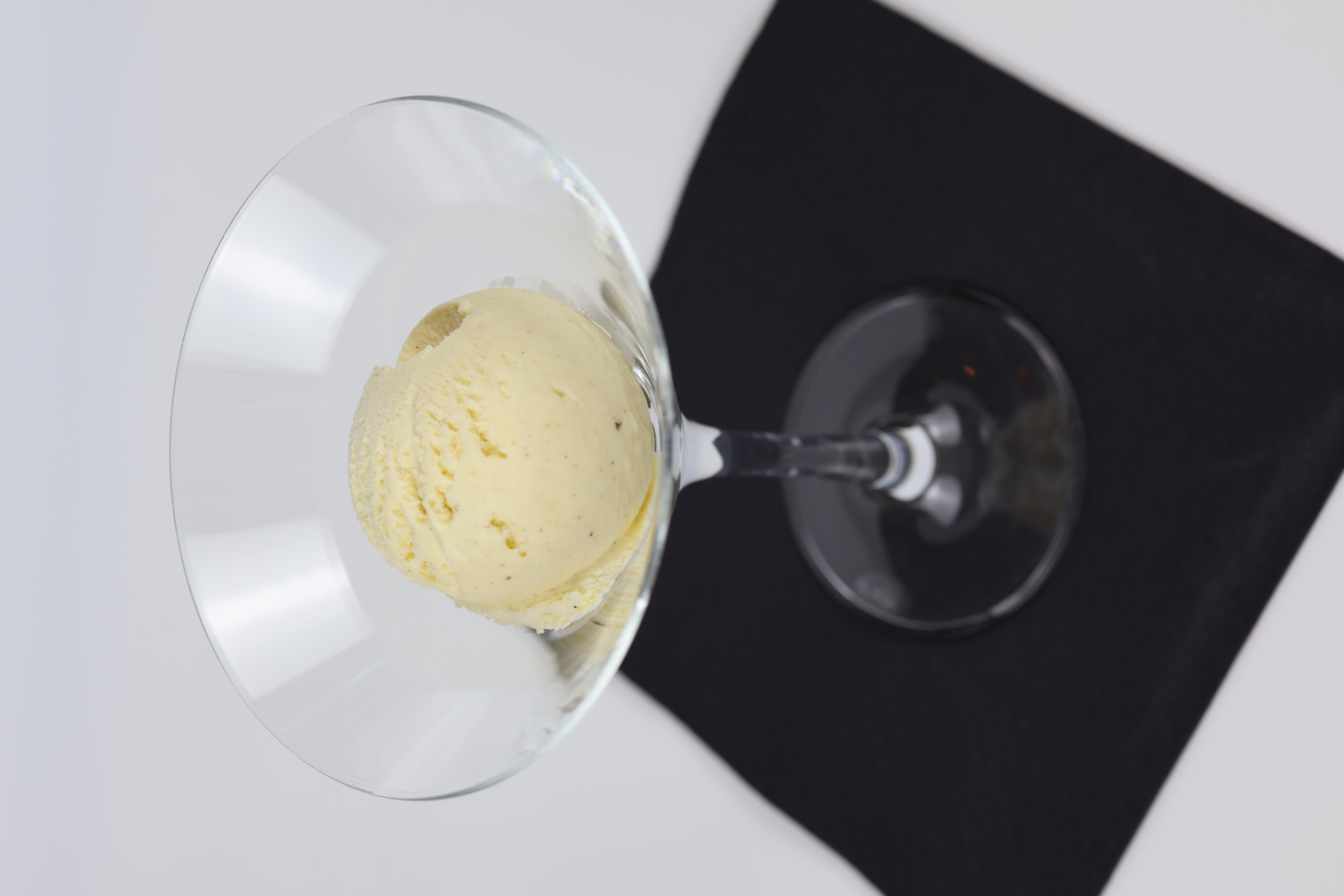 Eine Kugel hellgelbes Eis in einem Cocktailglas auf einem schwarzen Stoffuntersetzer