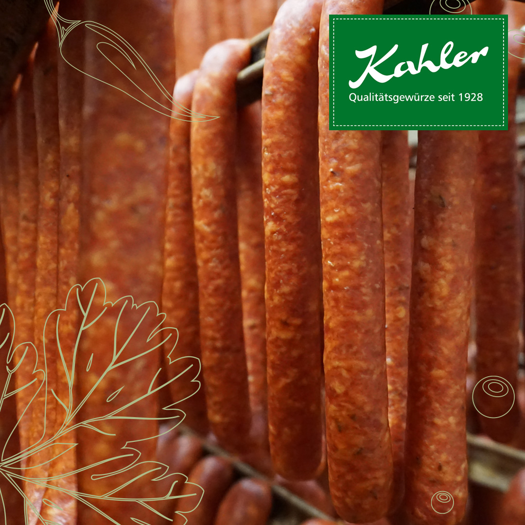 Mehrere lange, dünne Würste hängen nebeneinander an Metallstangen vor einem unscharfen Holzhintergrund, grünes Kahler Logo