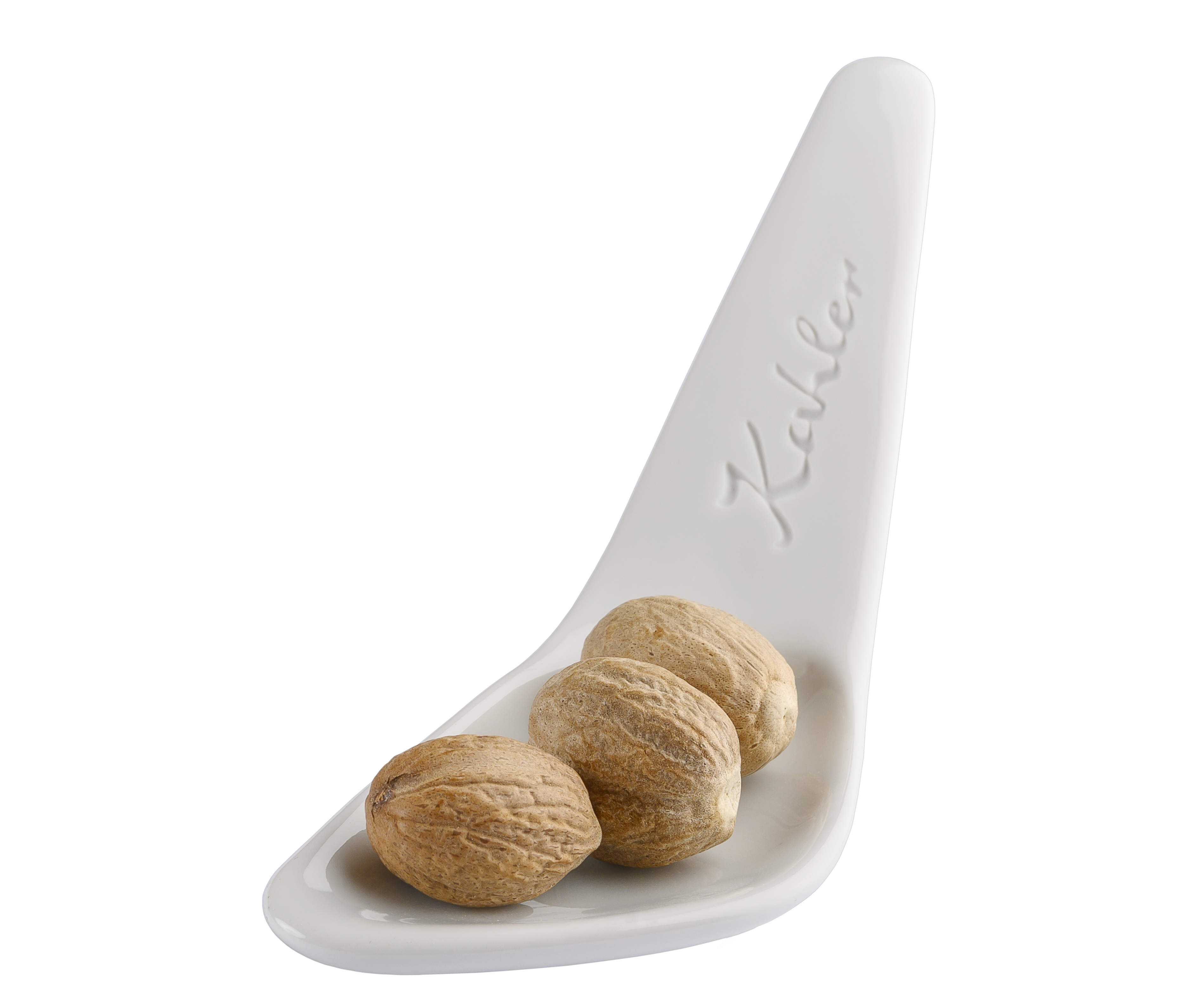 Drei ganze Muskatnuesse liegen auf einem weißen Keramikloeffel mit der Praegung "Kahler".