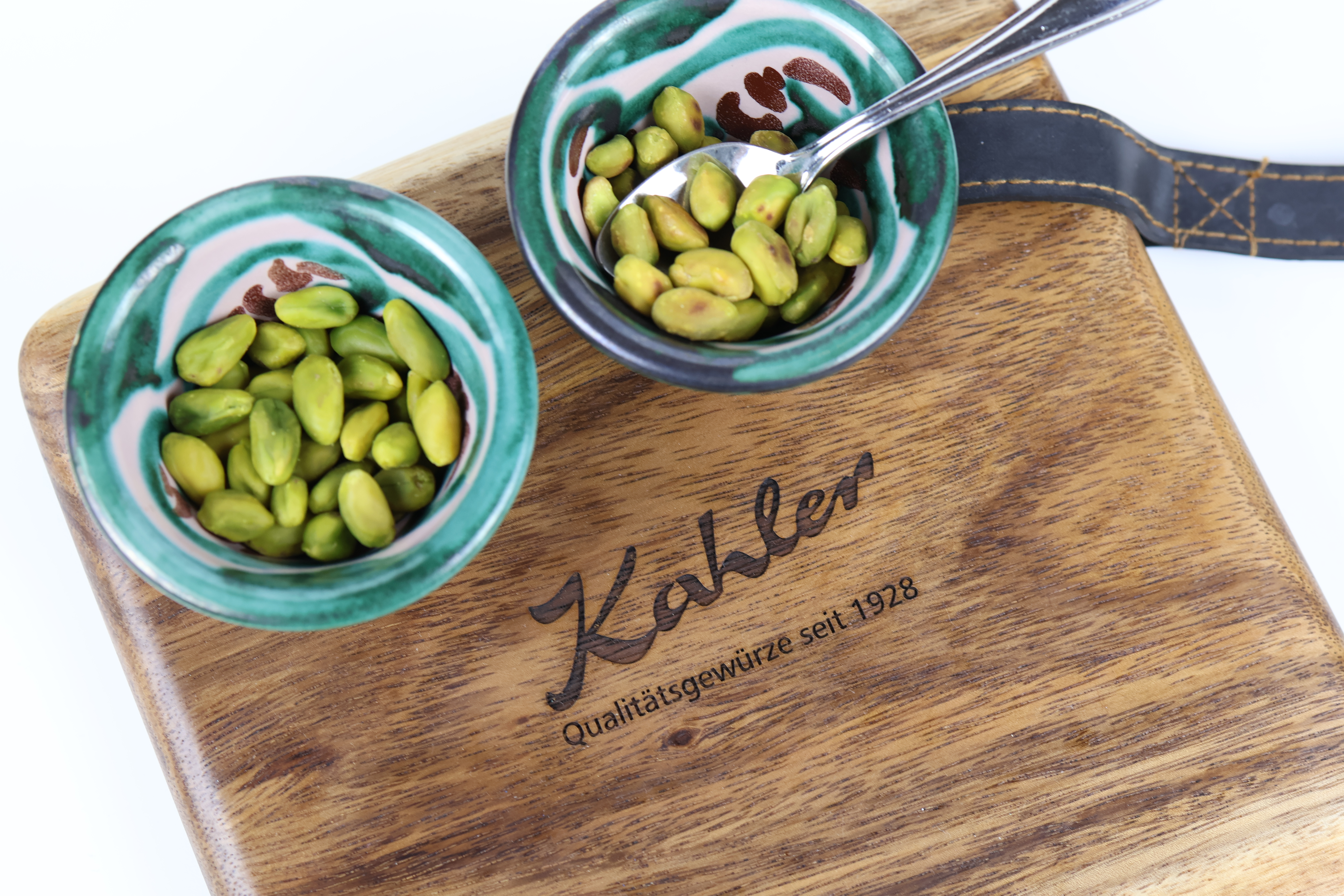Zwei kleine grüne Schalen mit Pistazien auf einem Holzbrett mit der Aufschrift 'Kahler Qualitätsgewürze seit 1928'