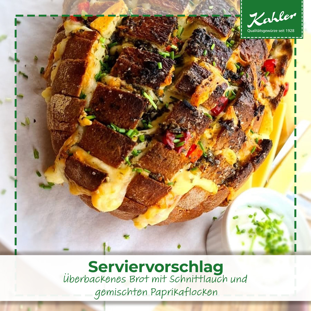 Überbackenes Brot mit geschmolzenem Käse, Schnittlauch und gemischten Paprikaflocken auf Backpapier mit kleinem Becher Schnittlauch-Dip und Kahler Logo