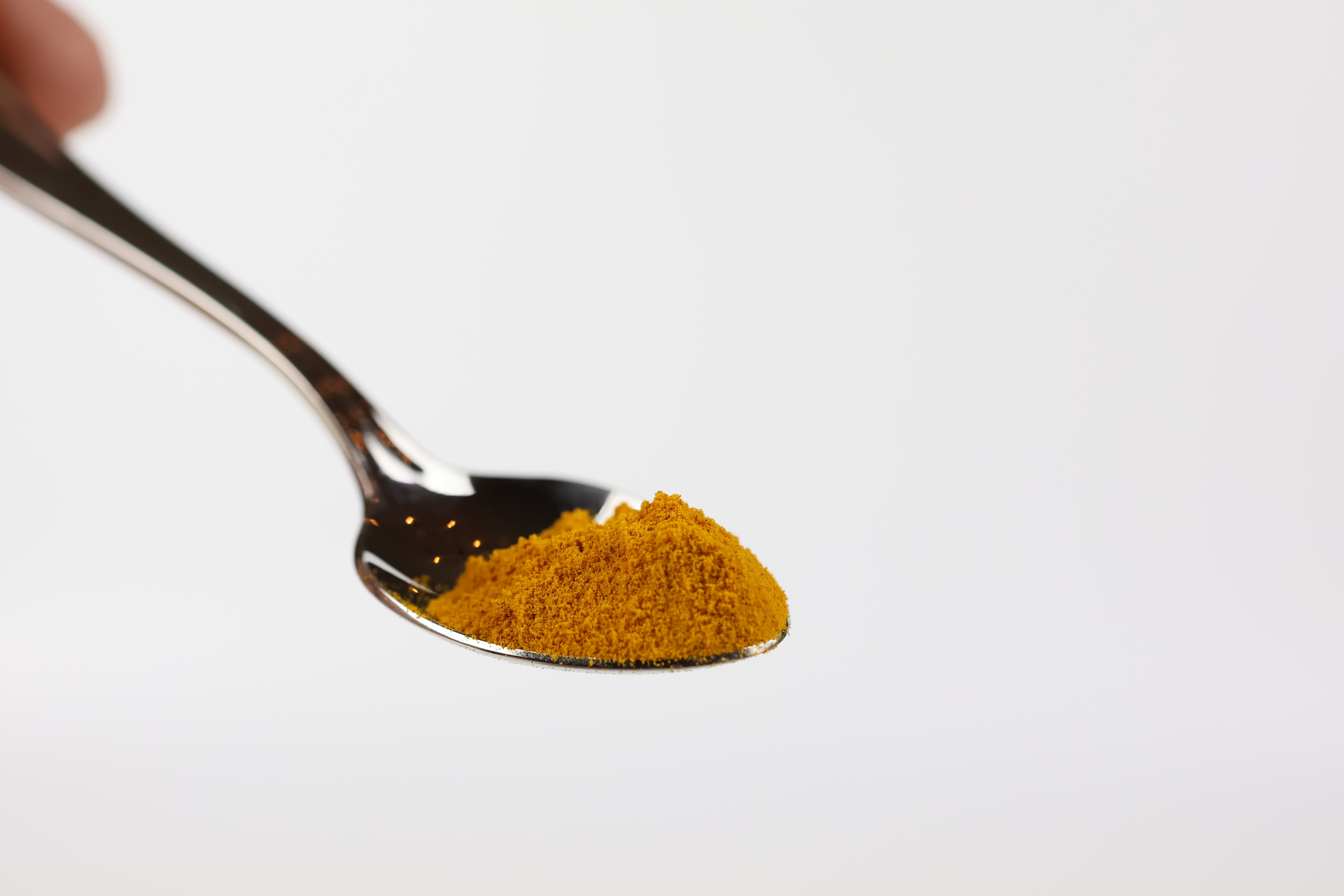 Löffel mit feinem gelb-orangefarbenem Curcuma Pulver von Kahler  vor weißem Hintergrund