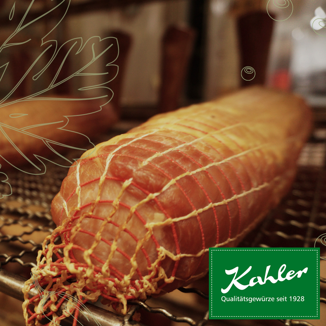 Ganze, in Netz gebundene Wurst auf einem Grillrost mit grünem Logo 'Kahler Qualitätsgewürze seit 1928'