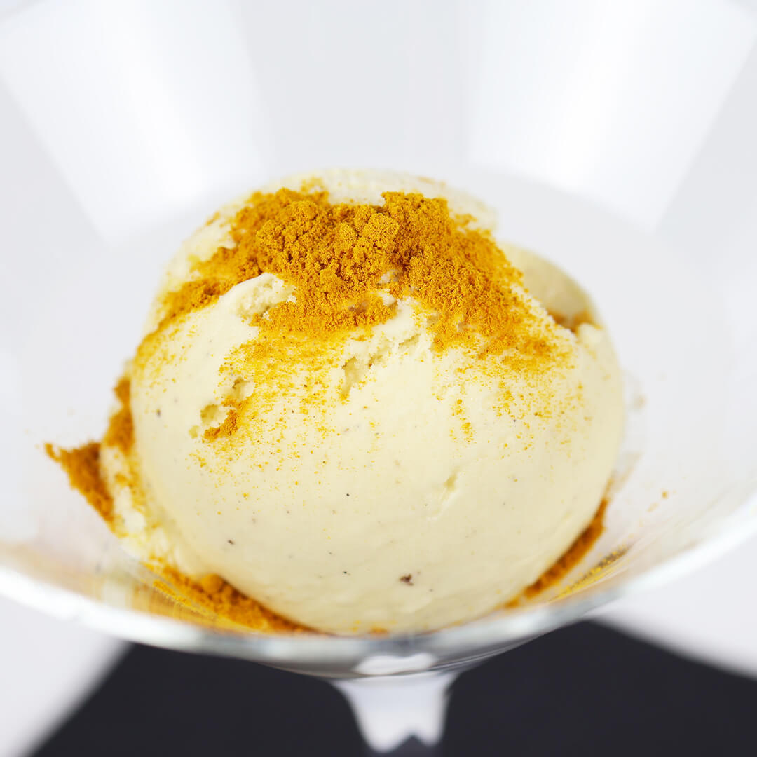 Kugel Vanilleeis in einem Glas mit einer Prise gelbem Gewürzpulver bestreut