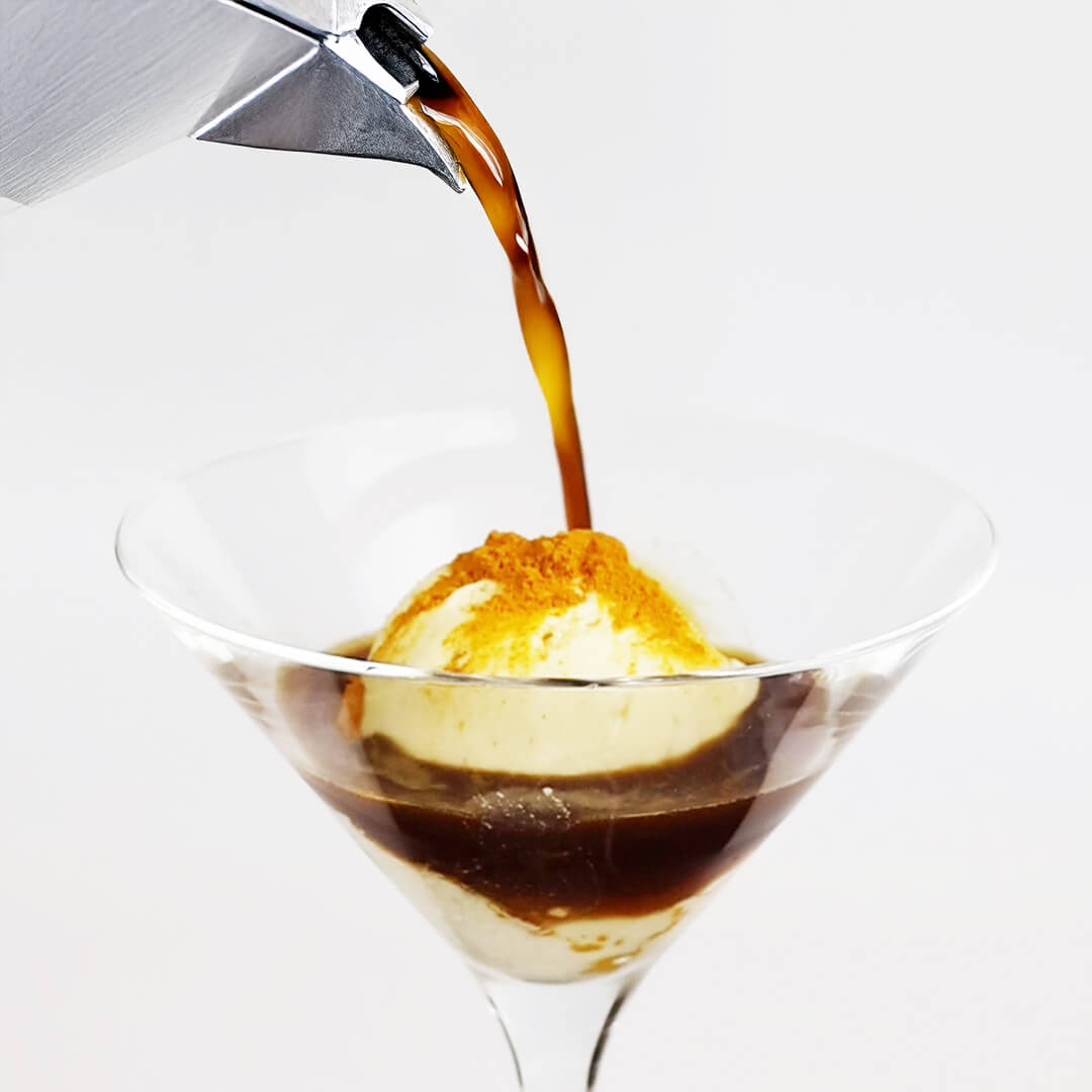 Espresso wird in ein Glas mit einer Kugel Vanilleeis und einer Prise Kurkumapulver gegossen